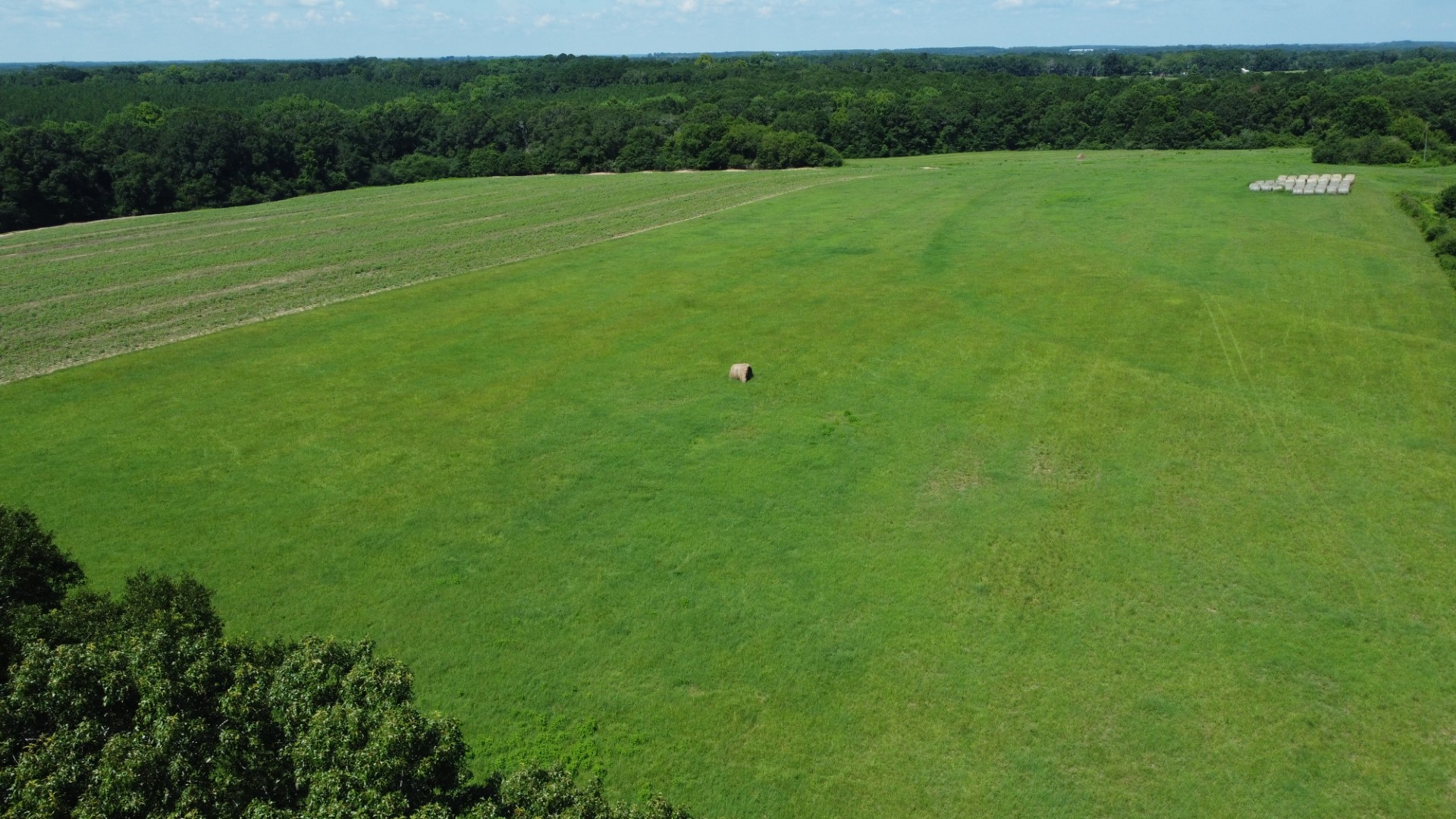 Aerial of the open ground with a single round bale and stacked bales in the distance