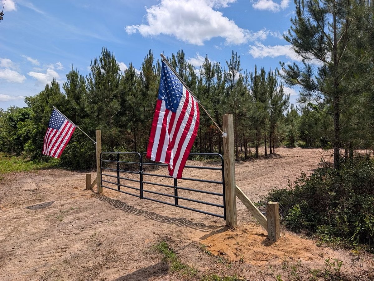 Gated entrance with American flags off paved Lovewood Road at Cypress Pines Mini Farm