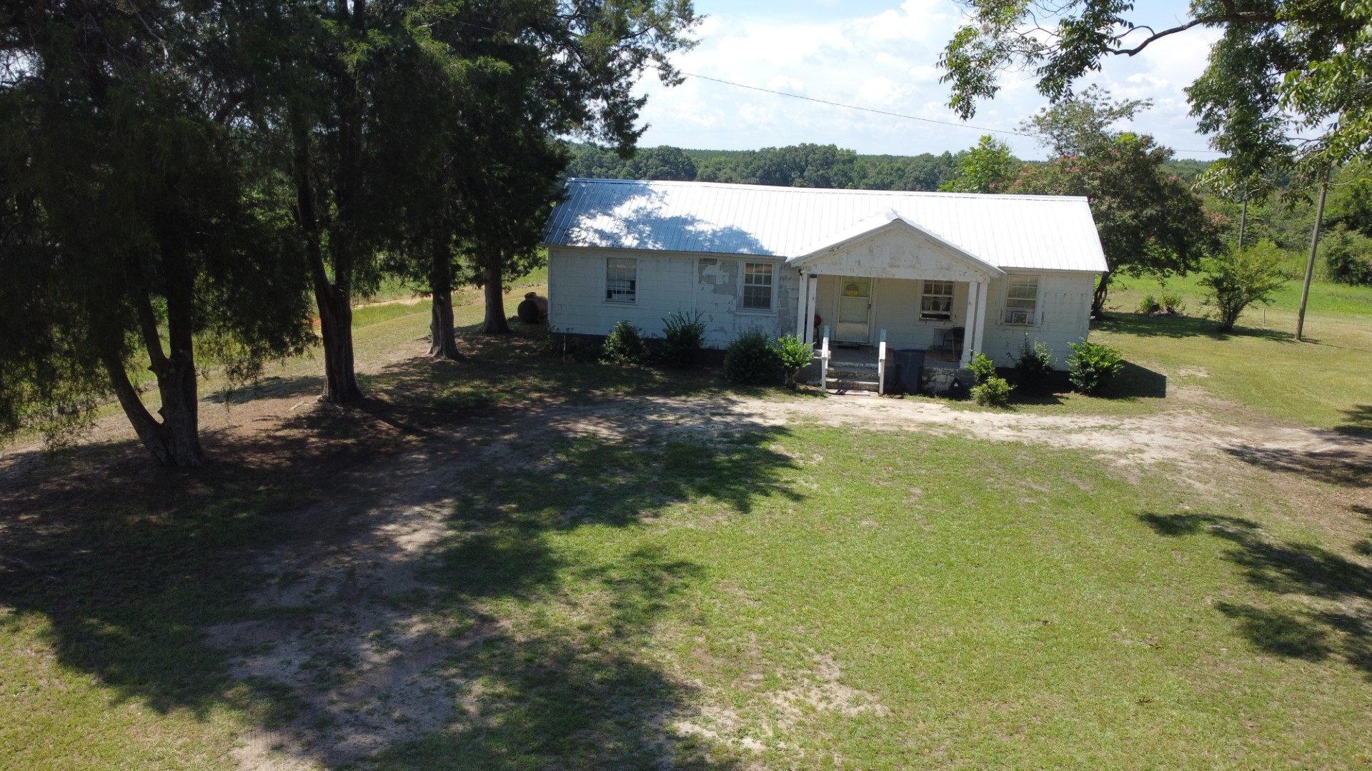 Low aerial of the white residence, dirt driveway and yard