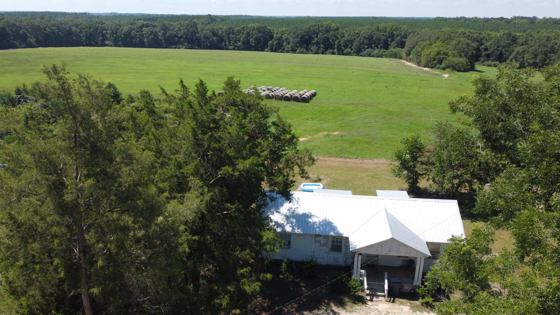 The white metal roof of the residence above the pasture and round bales