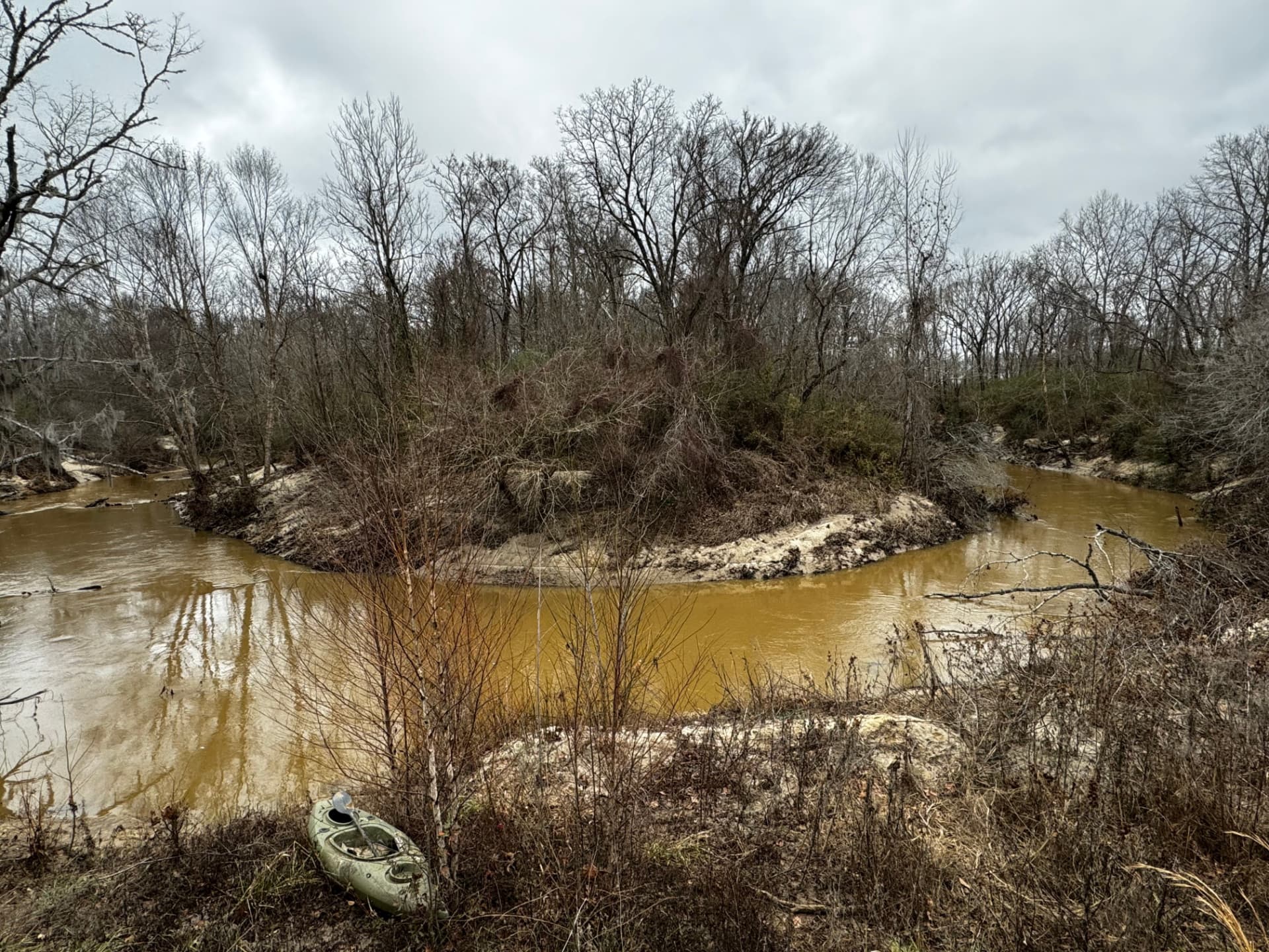 Bogue Chitto Creek bending around a wooded knoll, with a kayak pulled up on the bank